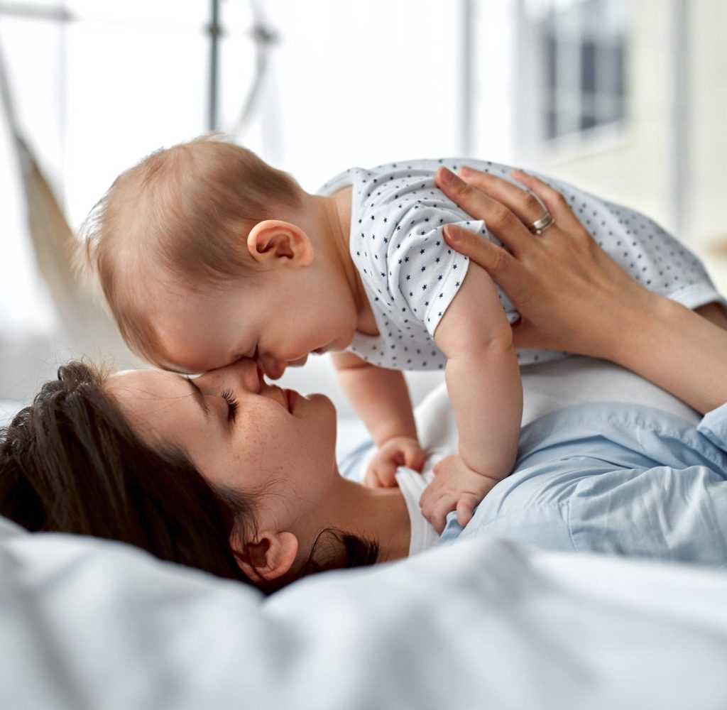 Loving mom carying of her newborn baby at home.Mom and baby boy playing in sunny bedroom. Parent and little kid relaxing at home. Family having fun together. Childcare, maternity concept.
